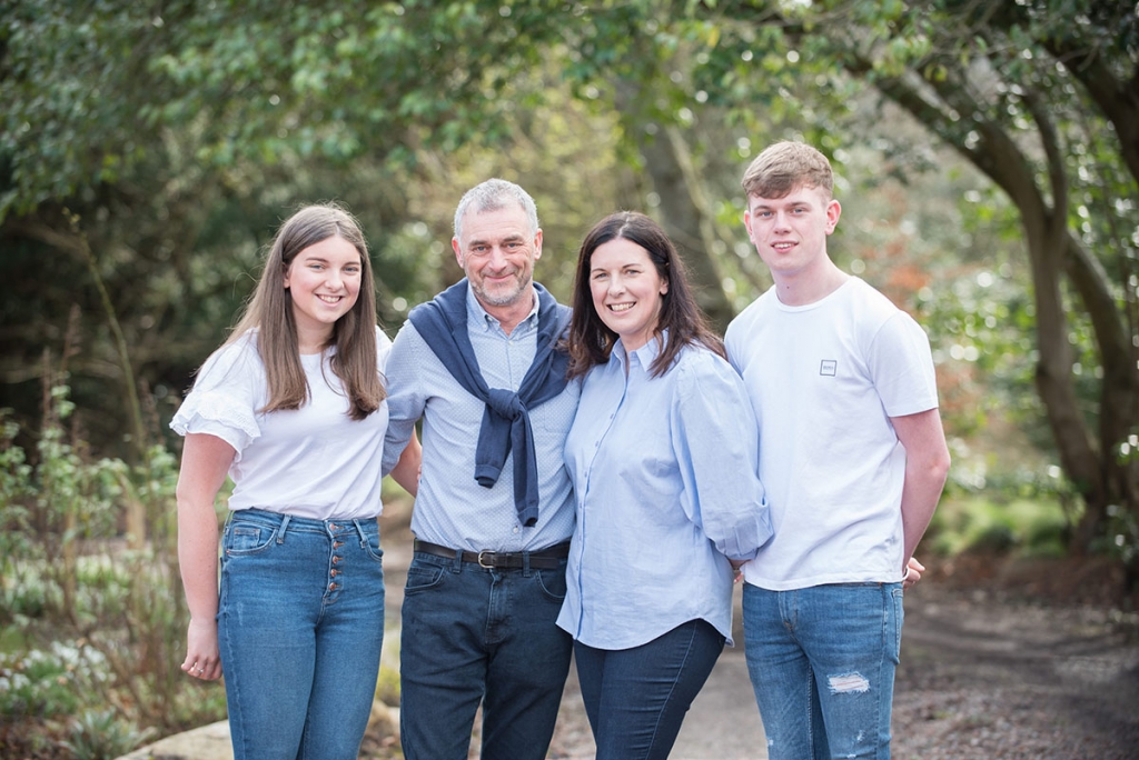 Parents and teenage son and daughter, all wearing blue and white, in a family photoshoot in woodland