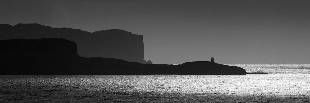 Isle of Skye photography - monochrome panorama of a small lighthouse on a peninsula overlooking the sea with cliffs behind