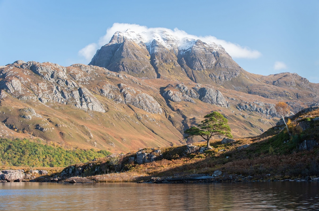 Torridon photography - mountain with snow and white cloud on its summit, with a tree in the foreground on the shore of a lake