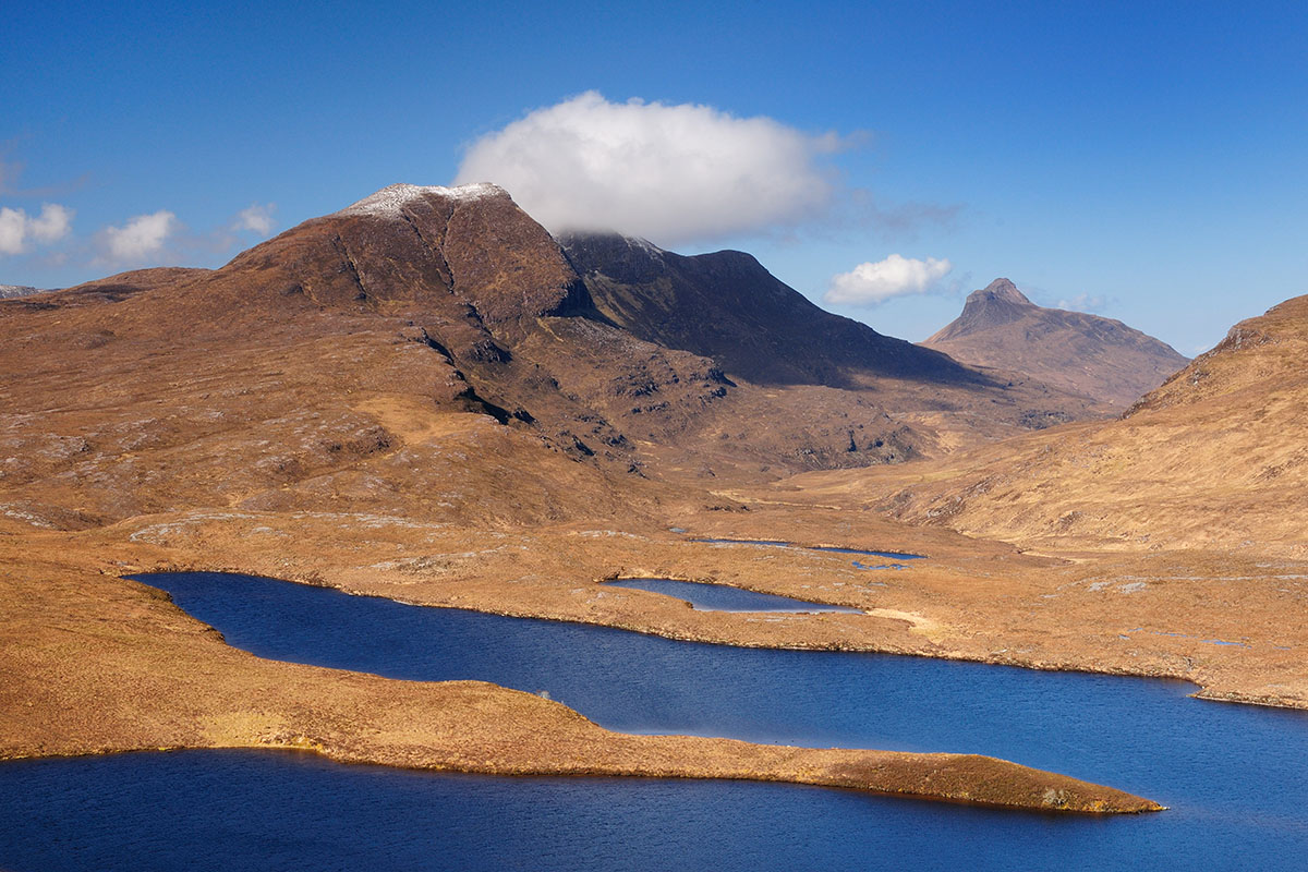 Ullapool things to do - mountains with white cloud on one of the summits, overlooking small lakes reflecting bright blue sky