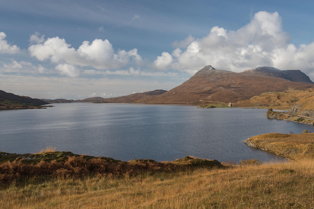 Ullapool things to do - lake overlooked by a mountain and a castle, under a blue sky with white clouds