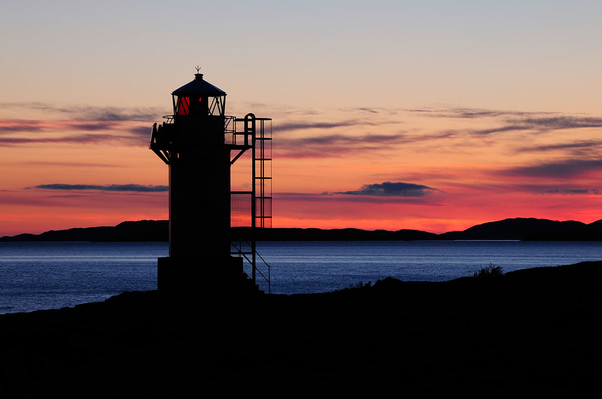 Ullapool things to do - small lighthouse silhouetted against a blue sea and a red sunset on the horizon