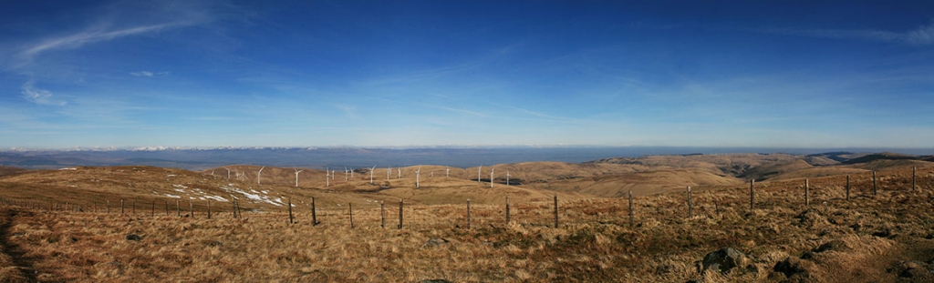 Wind farm photography - panoramic image of white wind turbines on a wide hill summit with a vivid blue sky overhead