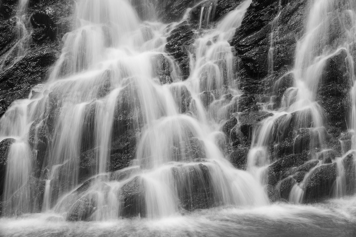 Black Isle photography - monochrome close-up of a waterfall with water flowing over dark rock in slow motion