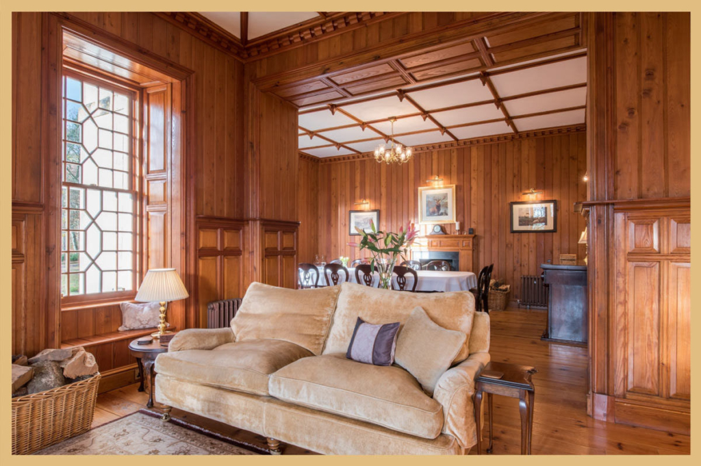 Interior photograph of a luxurious cream couch in a wood paneled room with a white ceiling and window on the left