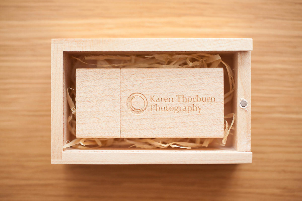 A light wooden USB drive engraved with the text 'Karen Thorburn Photography', placed in a matching wooden box