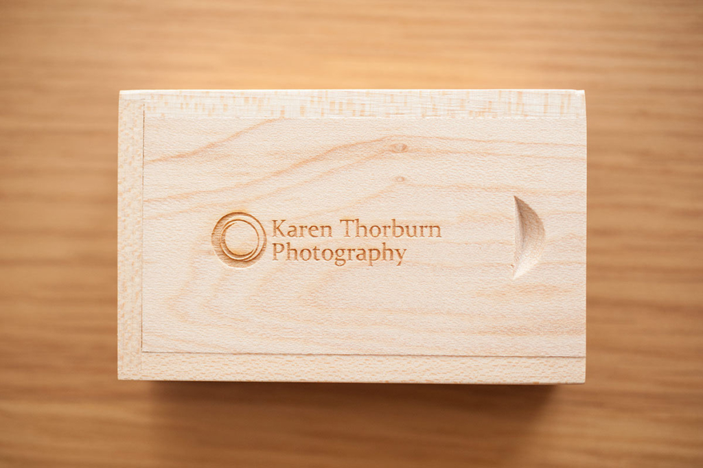 A light wooden box engraved with a circular logo and the text 'Karen Thorburn Photography', placed on a wooden table surface