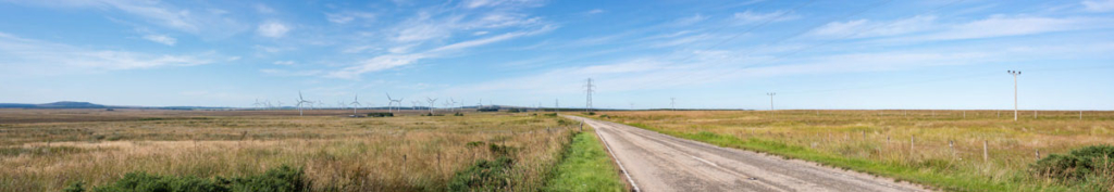 Panoramic landscape photograph of the A9 trunk road leading towards a wind farm and pylons, shot in sunny conditions