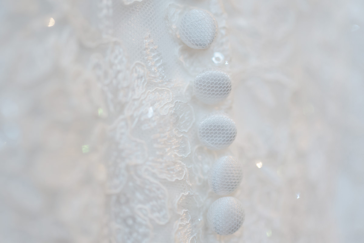 Detail of five white buttons on the back of a wedding dress with sequins reflecting the light