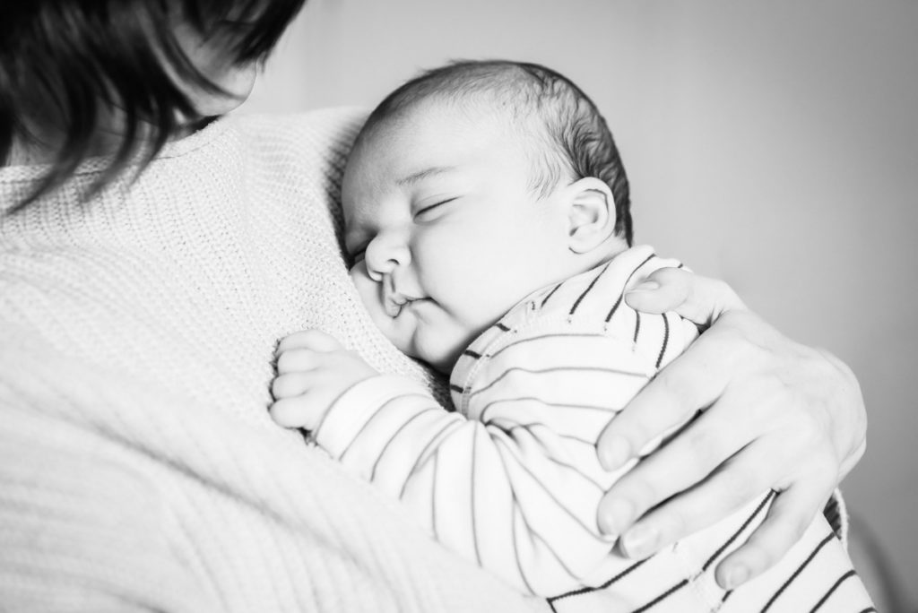 Black and white of a sleeping baby in a striped top held in the arms of a woman in front of a white background