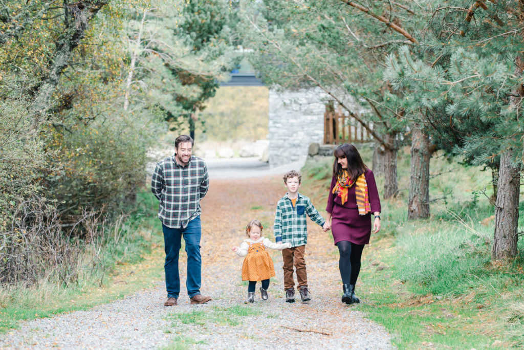 Parents and their school-age son and infant daughter walking on a gravel track in a woodland during a family photoshoot