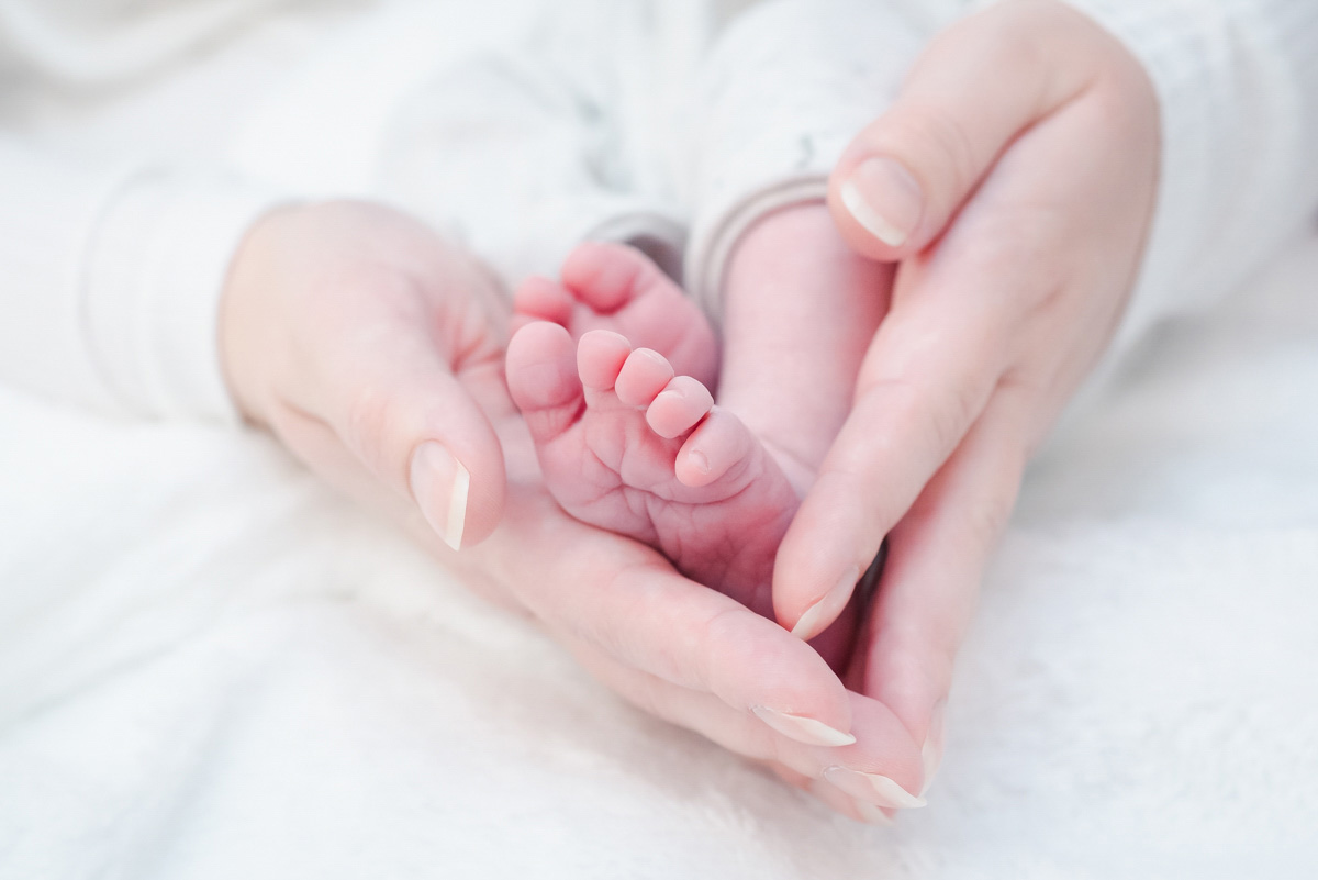 Close-up of a baby's foot held in the hands of a woman with manicured nails with a soft white background
