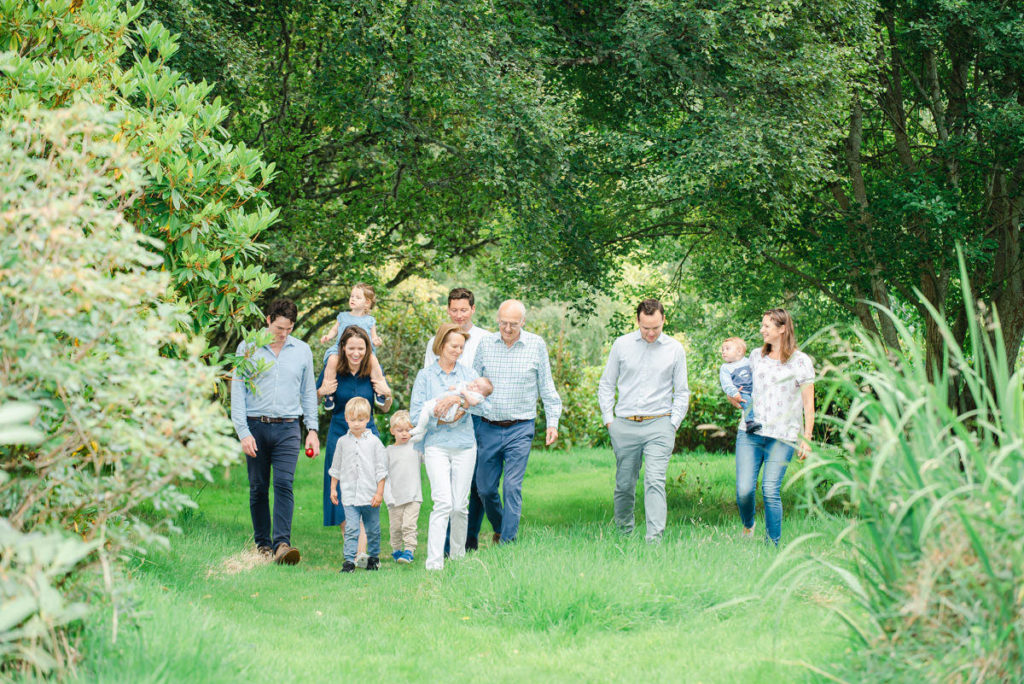 An extended family of seven adults and four children and a baby walking through lush green grass in a garden with trees