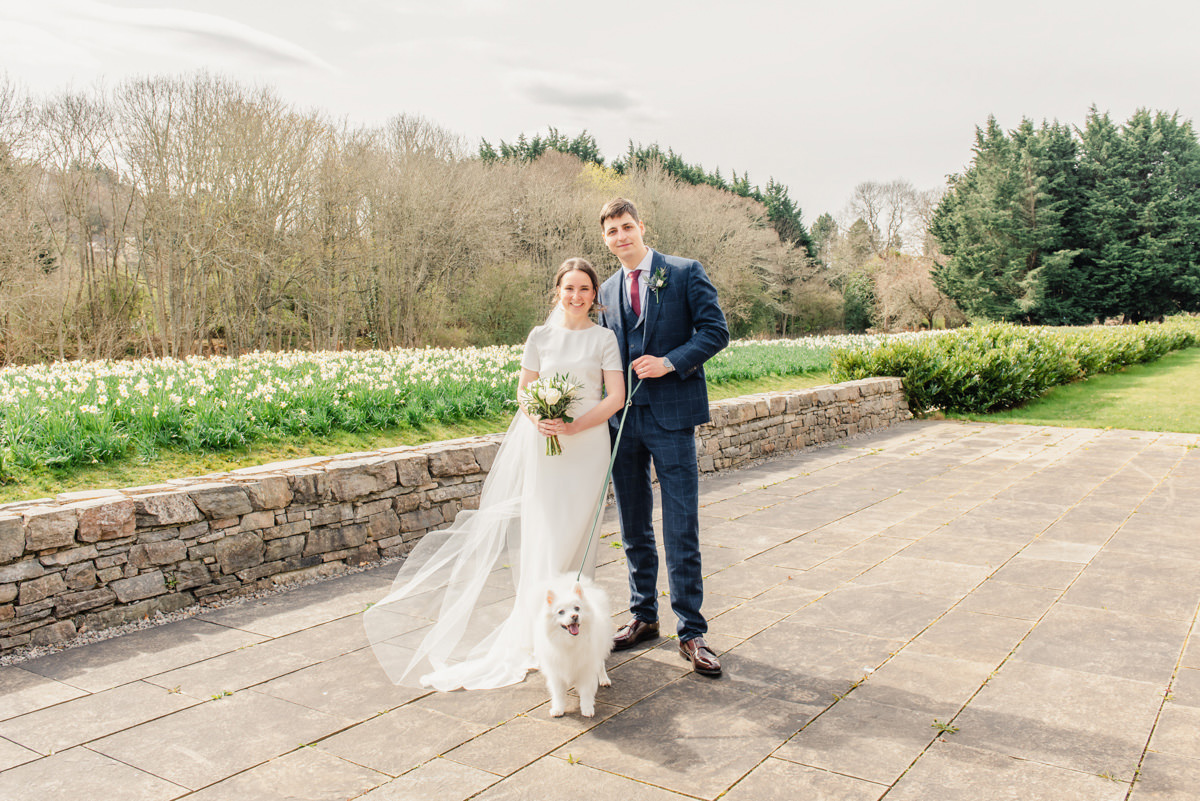 A bride a in a long veil stands by her groom with a white dog at their feet outside the Highland Archive centre in Inverness