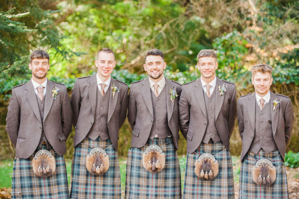 A groom and four groomsmen dressed in kilts with gold ties stand in a woodland setting on Abercairny Estate near Crieff