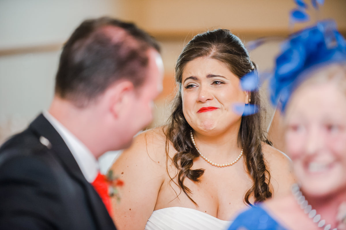 A bride with red lipstick and long brown hair looks emotionally at a guest during the wedding speech in Broughty Ferry