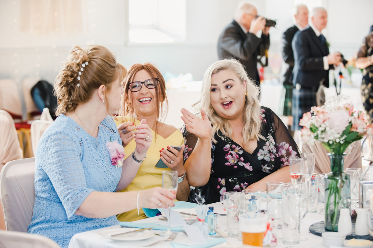 Three seated female wedding guests share a funny moment during the speeches at a wedding in Cromarty