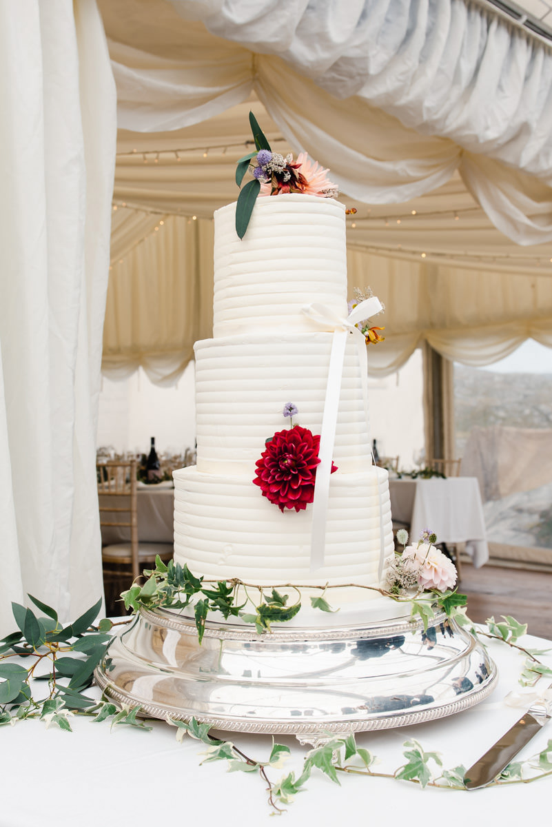 A white wedding cake with a red rose decoration sits on a silver platter with ivy around its base at a Lochinver wedding