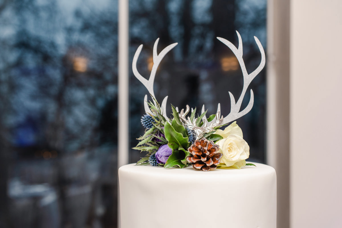 A cake topper in the image of stag antlers surrounded by floral cake decoration on a white wedding cake at Logie Country House