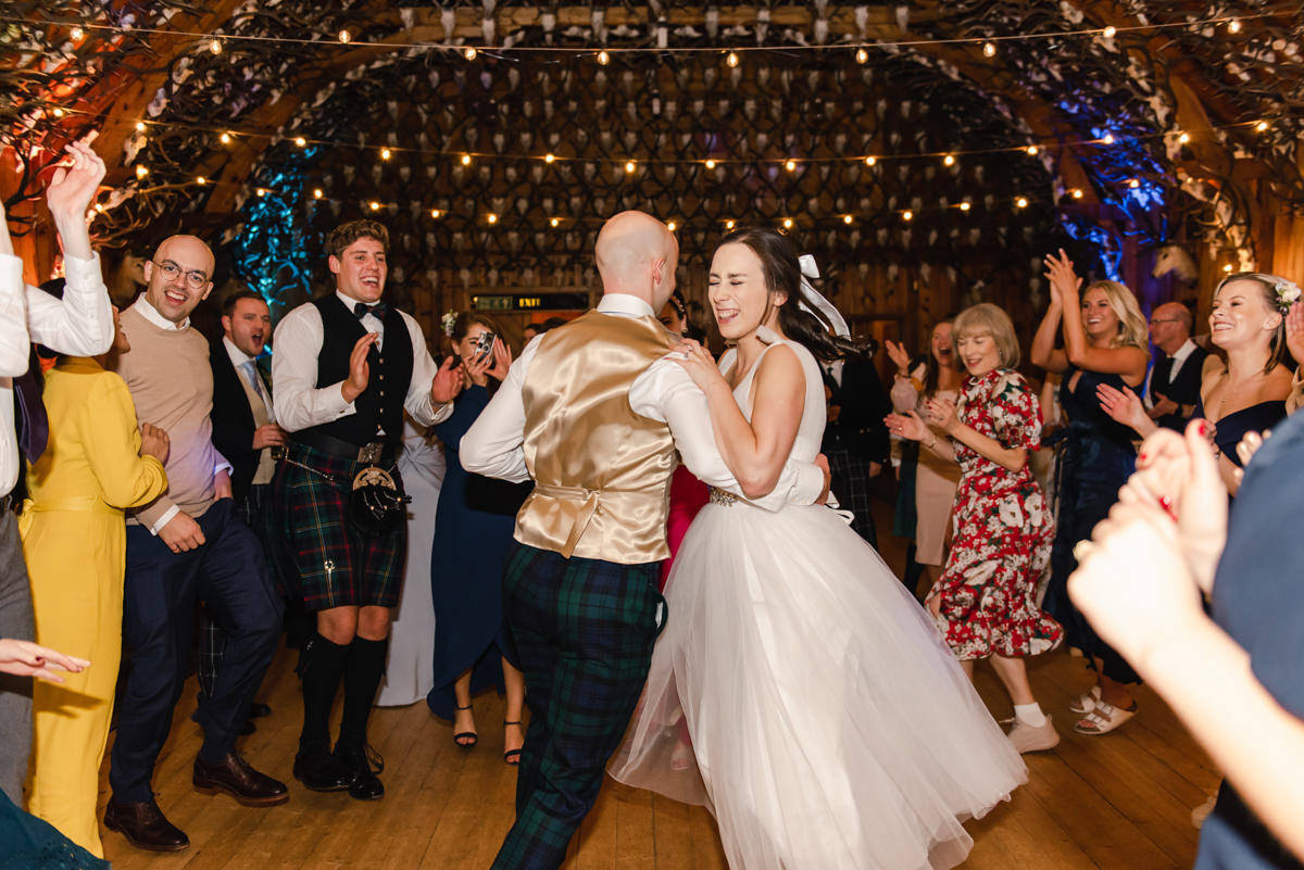 A wedding couple dance a jig as the guests clap in a circle around them at Mar Lodge near Braemar