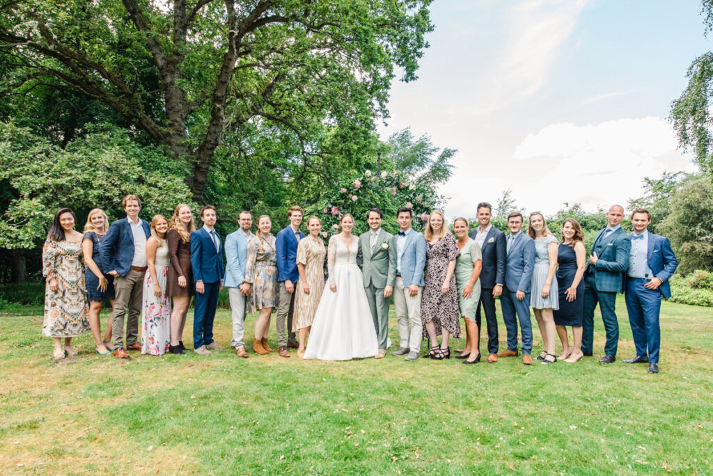 A large wedding group with the bride and groom standing under a floral arch on the lawn of Pitcalzean House near Tain