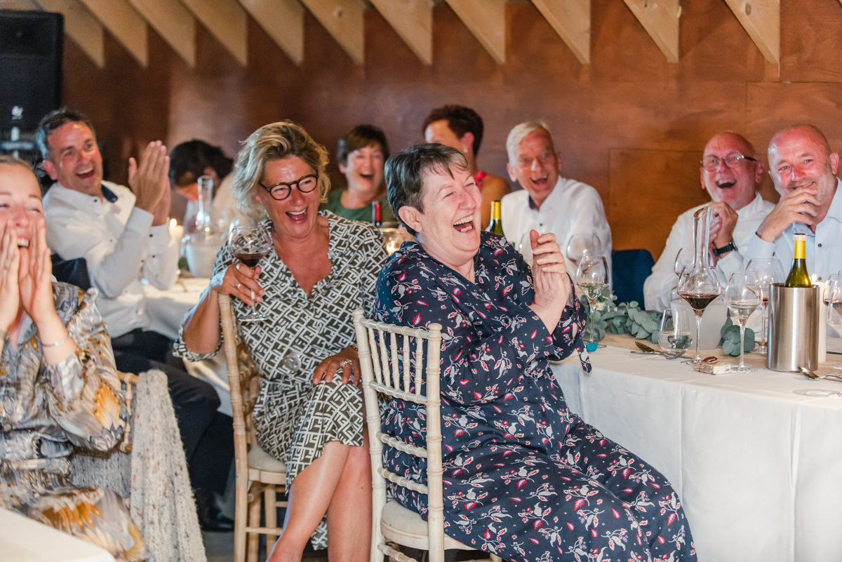 Seated wedding guests at a large table drink wine, clap and laugh during the speeches at Pitcalzean House