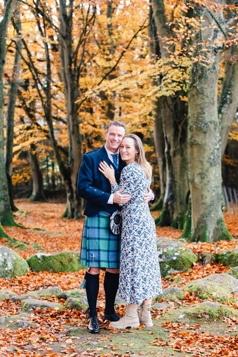 A couple embrace in a autumnal beech woodland setting while celebrating their engagement