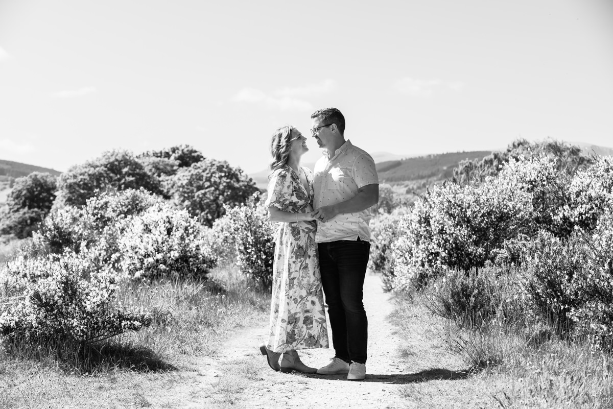 A black and white image of a couple on a country track surrounded by gorse bushes staring lovingly into each others eyes