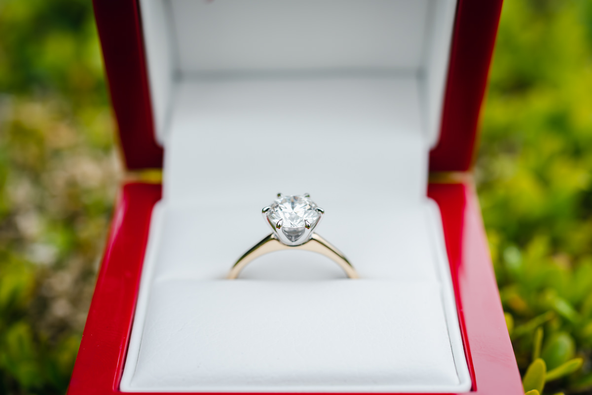 Close up of an engagement ring with a large diamond in a red presentation box with a green background
