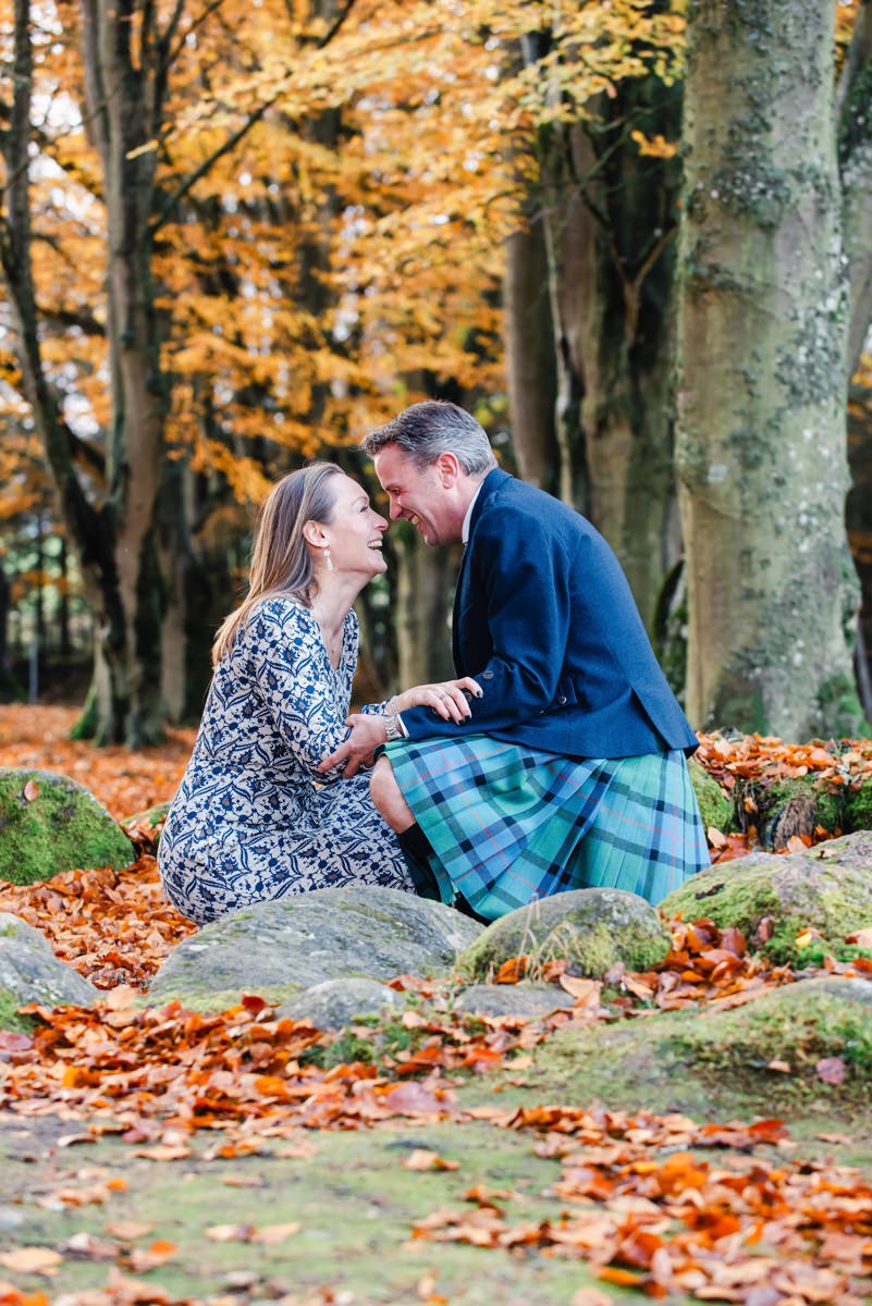 In an autumnal woodland setting a formally dressed couple kneel in the middle of a stone circle and share a tender moment