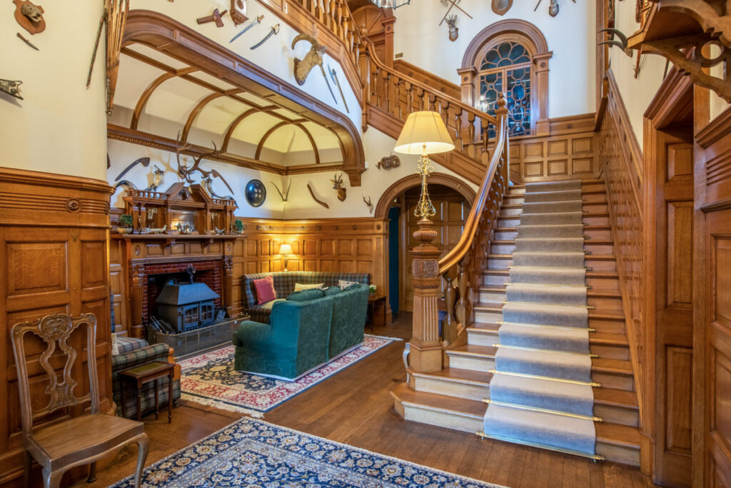 A vintage wooden staircase with white walls adorned with vintage weapons and deer antlers.