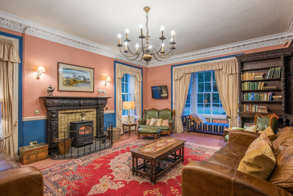 A vintage drawing room with peach coloured walls, blue window frames, wood burning stove and a brown leather sofas