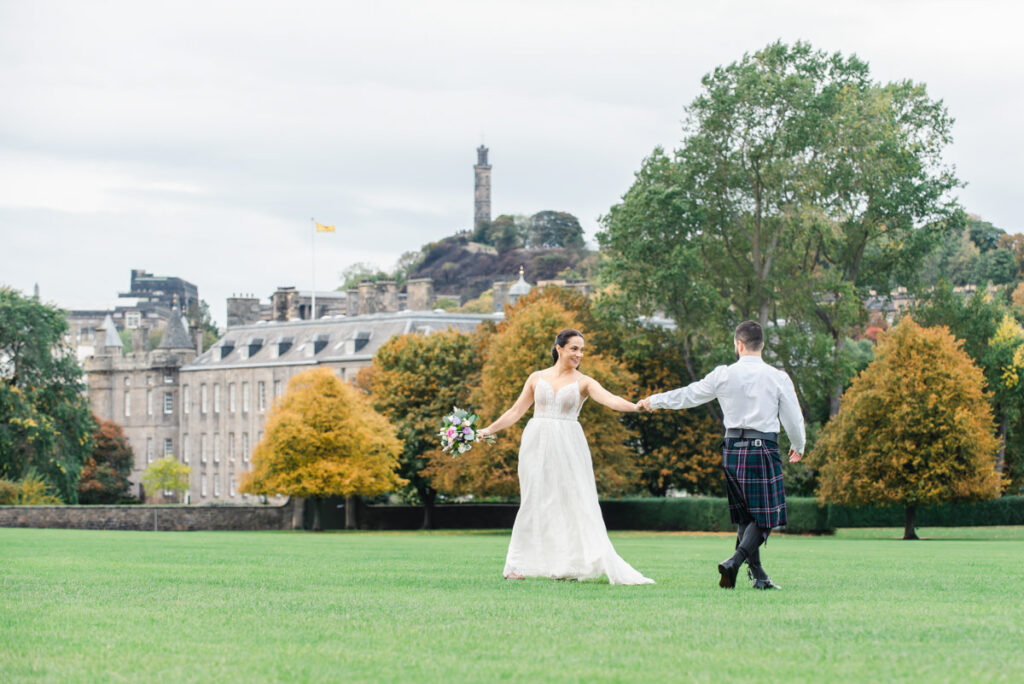 In a large grassed urban park setting with Georgian tenements in the background a bride and groom share a dance