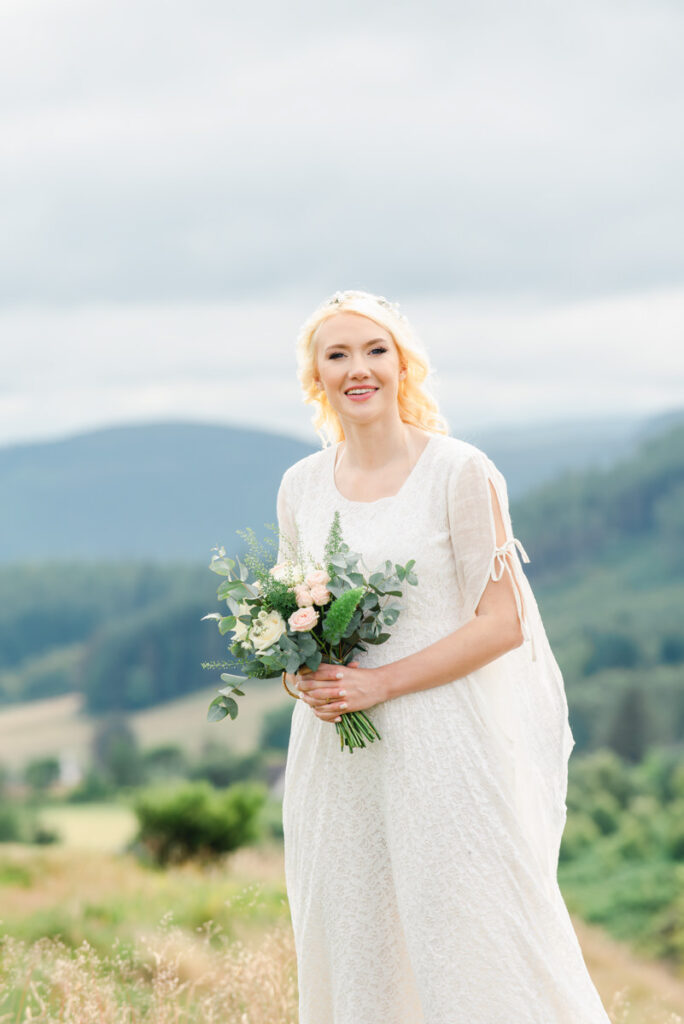 A blonde bride in a long flowing traditional white wedding dress holds her bouquet of white and pink roses