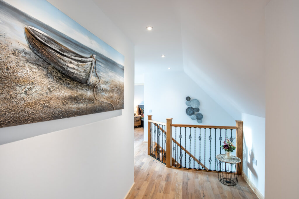 A large painting of a row boat hangs on the white walls of a hallway that has a staircase with a wooden handrail