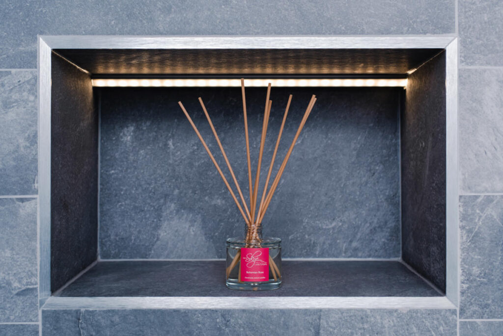 Incense sticks in a a clear jar with a pink label positioned in the centre of a slate grey alcove