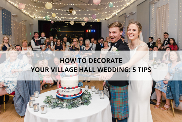 A bride and groom cutting a wedding cake in front of guests in a village hall